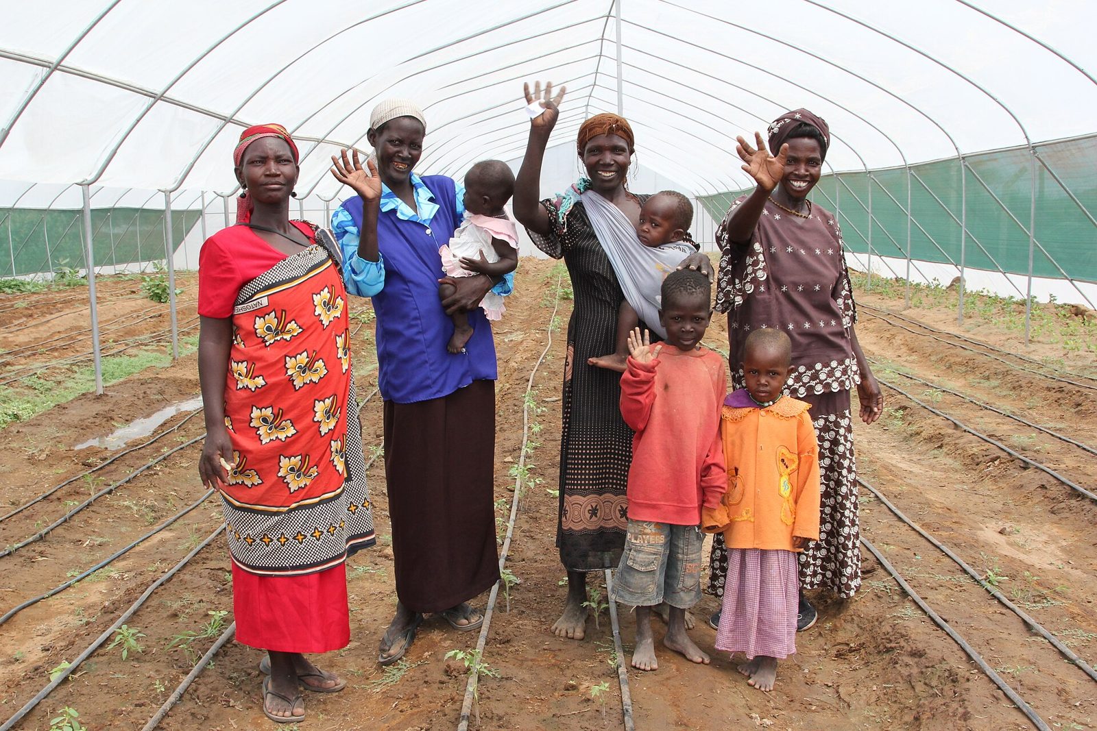 Women of a mothers' support group with their children in their greenhouse, waving
